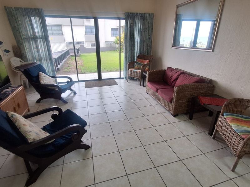 A spacious living room featuring neutral tiled flooring and large sliding glass doors that provide direct access to the outdoor garden area.
