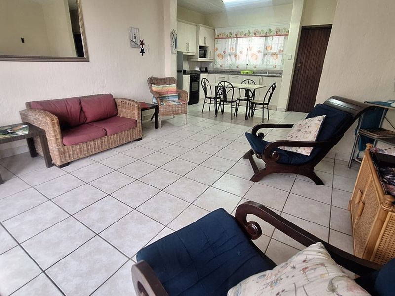 Open-plan living and dining area featuring tiled flooring and a functional kitchen with built-in cabinetry and appliances.