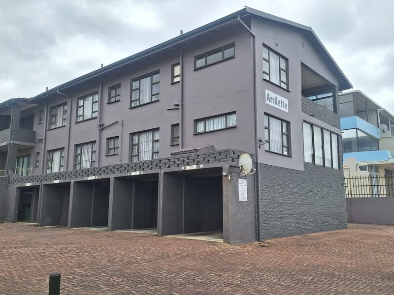 Exterior view of the Arrilette apartment complex featuring a paved driveway and multiple covered parking bays.