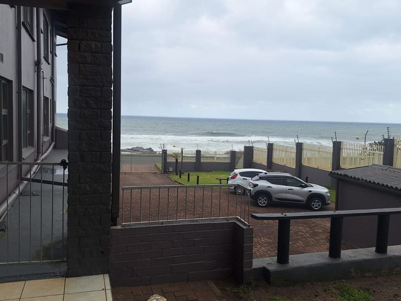 Rear exterior view of the apartment building featuring a paved driveway, boundary wall with electric fencing, and direct ocean views.