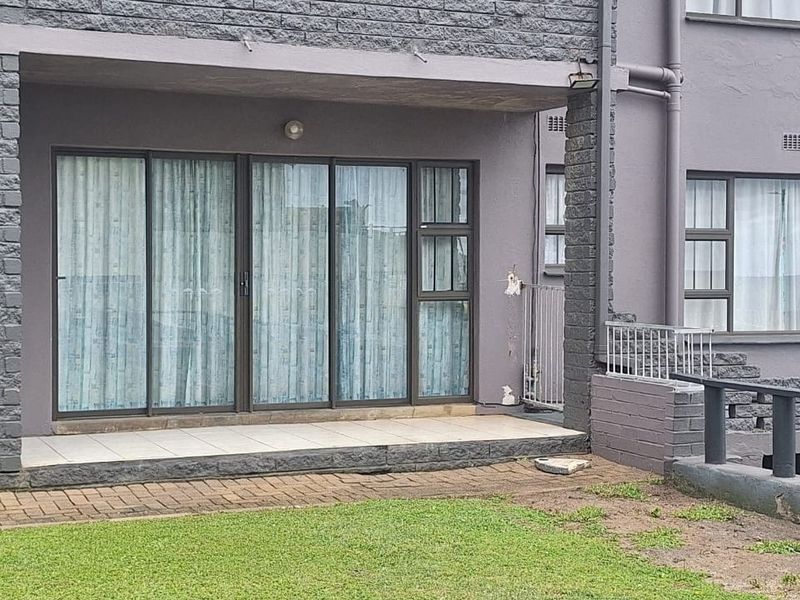 Ground floor apartment exterior featuring a tiled patio area with sliding glass doors and access to a shared garden space.
