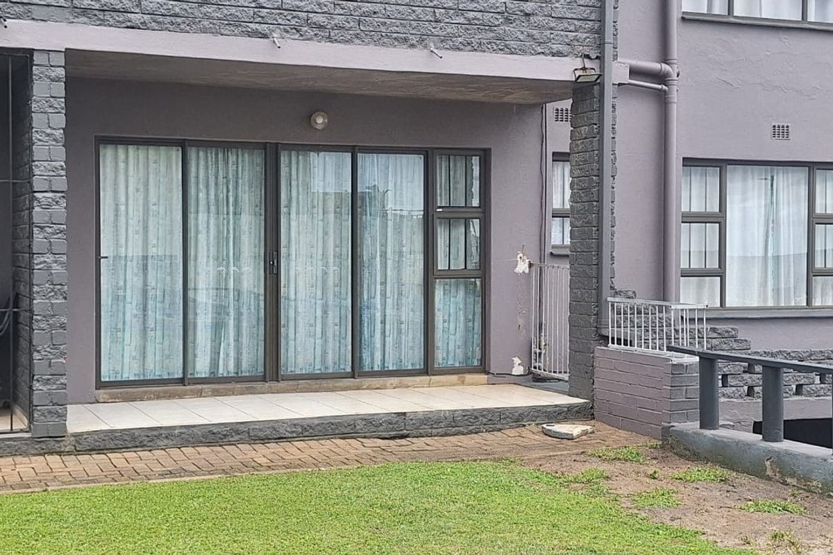 Ground floor apartment exterior featuring a tiled patio area with sliding glass doors and access to a shared garden space.