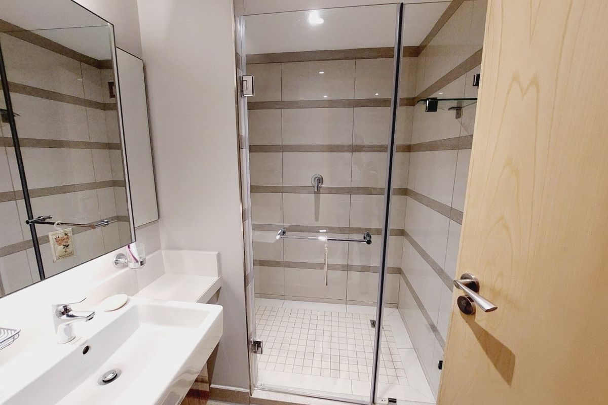 A modern, well-maintained bathroom featuring a walk-in shower with glass enclosure, wall-mounted basin, and neutral tiled finishes.
