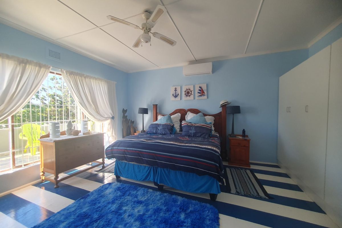 A spacious bedroom featuring a ceiling fan, split-system air conditioning, and built-in wardrobes, with large windows fitted with security bars.
