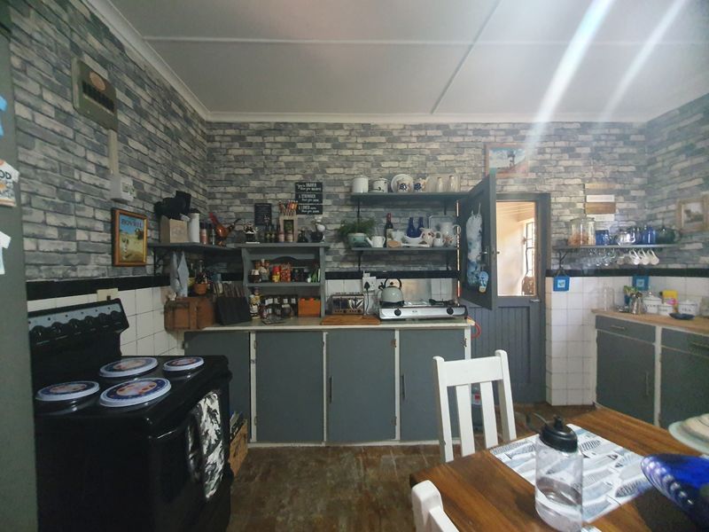 A rustic-style kitchen featuring grey cabinetry, brick-patterned wallpaper, tiled splashbacks, and a freestanding stove, offering a functional but dated culinary space.