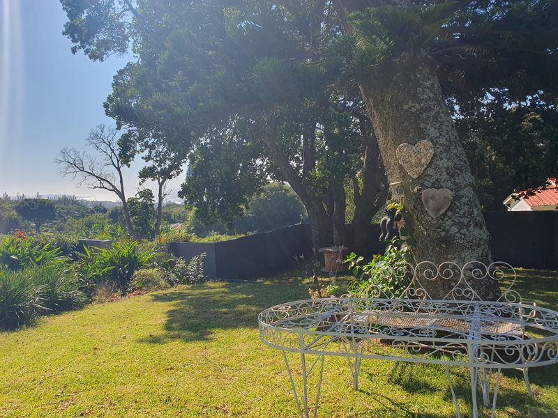 A peaceful, well-maintained garden area featuring mature trees, a lawn, and a retaining wall with scenic views.