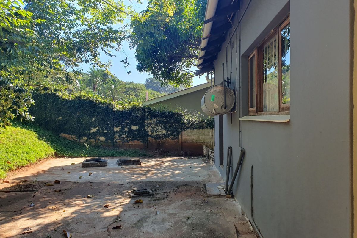 Rear exterior view of the property featuring a concrete patio area, external geyser, and mature garden surroundings.