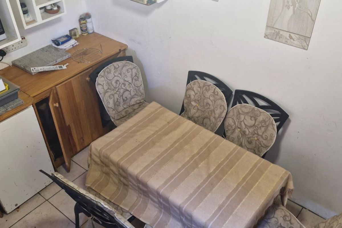 A compact kitchen area featuring built-in cabinetry, tiled flooring, and a dining space, showing signs of wear and dated finishes.
