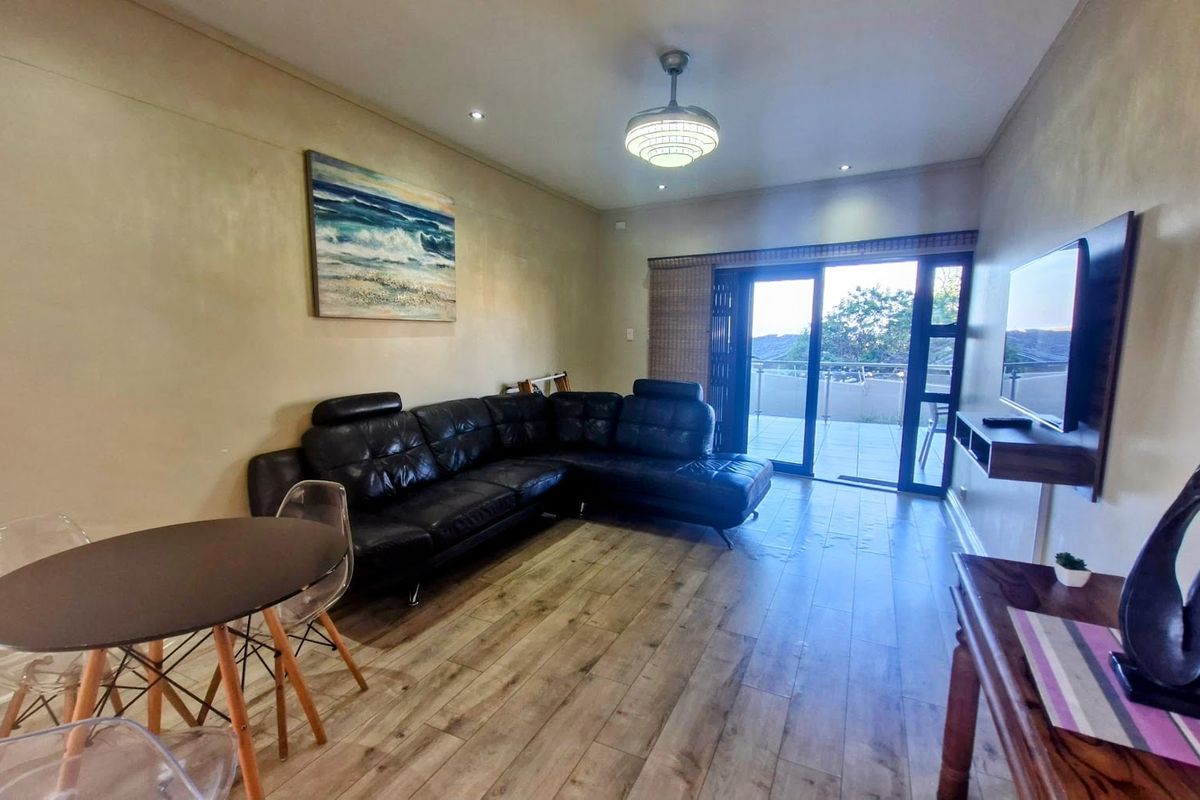 Spacious living room featuring wood-look tile flooring, recessed lighting, and large sliding glass doors providing access to the balcony.