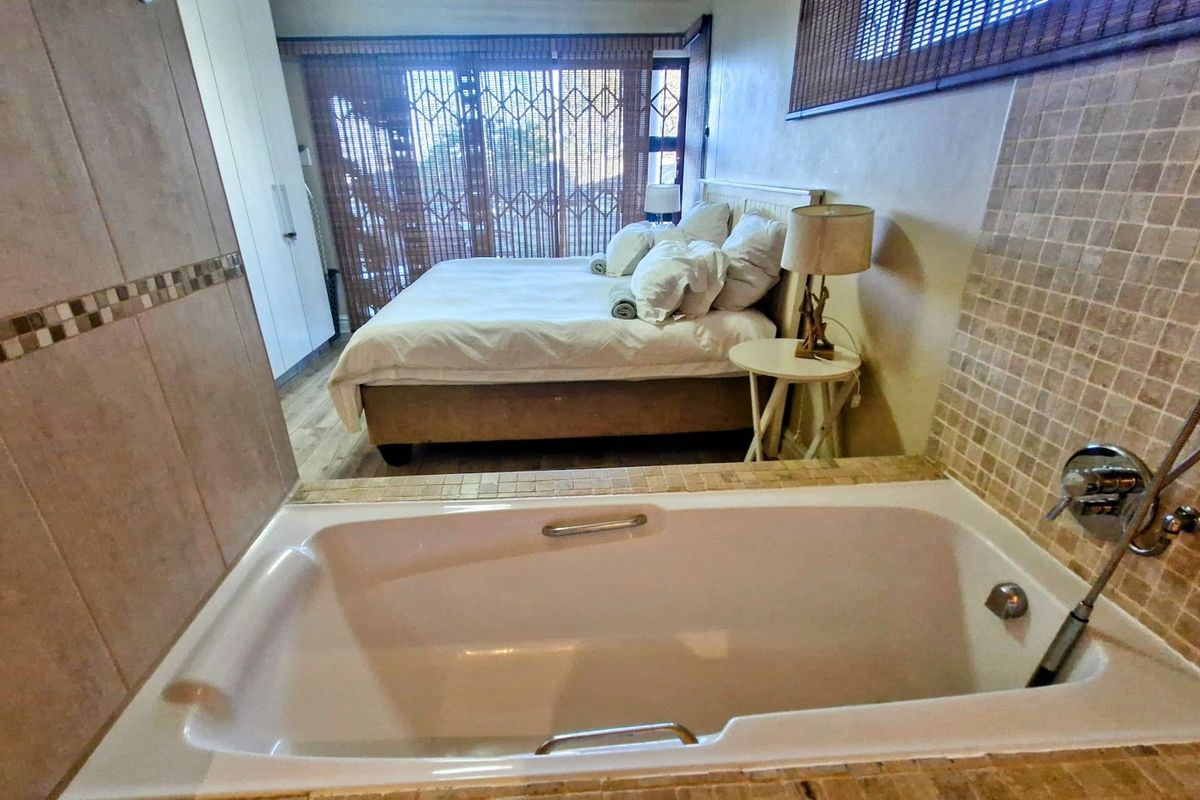 Bedroom featuring an open-plan en-suite bathtub, built-in wardrobe, and laminate flooring with access to a balcony through a security gate.