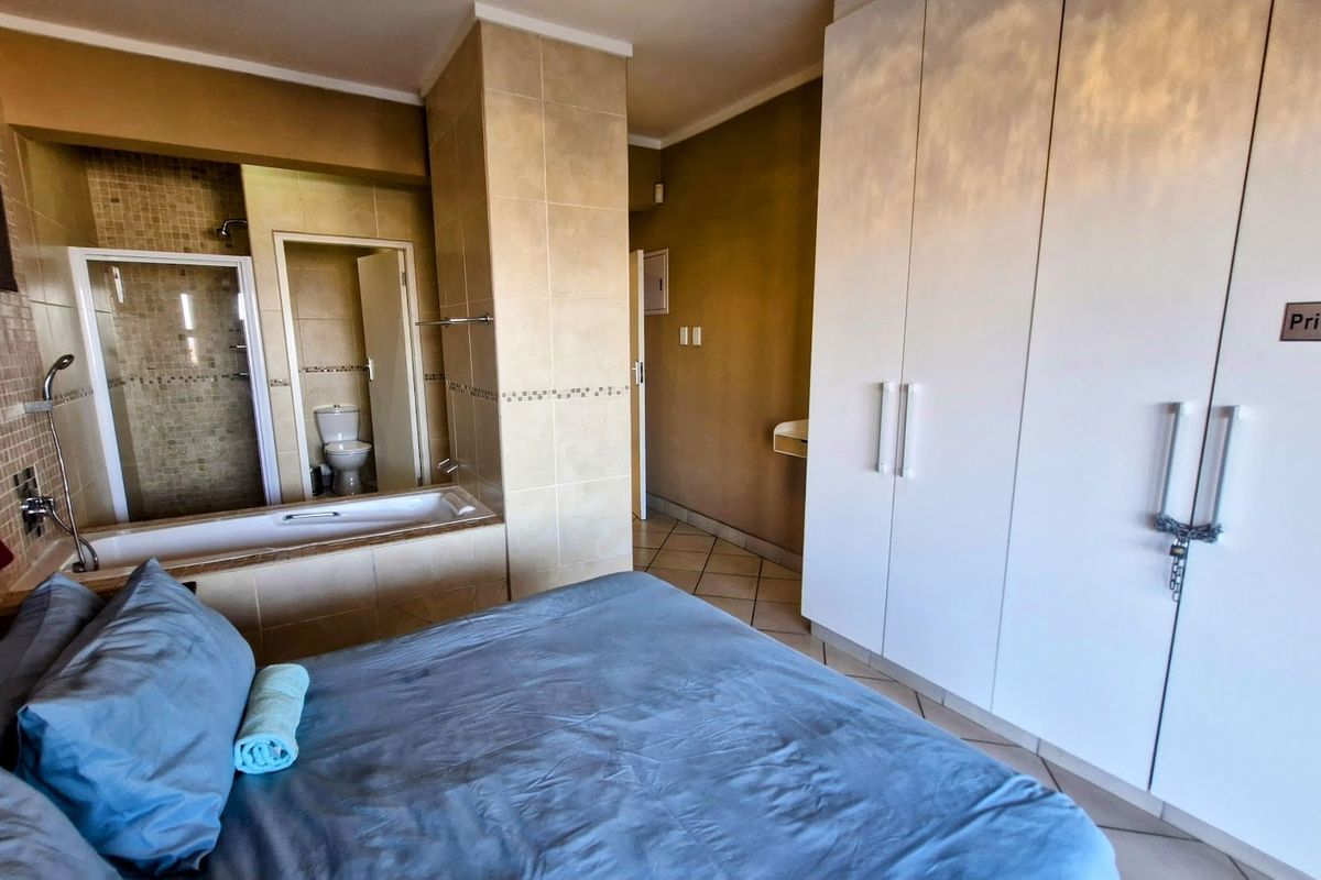 Bedroom featuring an open-plan en-suite bathroom with a tiled bathtub, shower, and toilet, complemented by built-in wardrobes and tiled flooring.