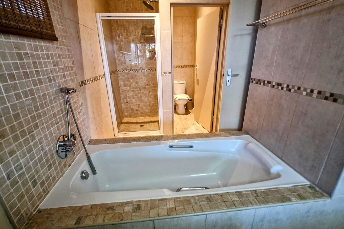 A tiled bathroom featuring a built-in bathtub, a separate glass-enclosed shower, and a private toilet area.