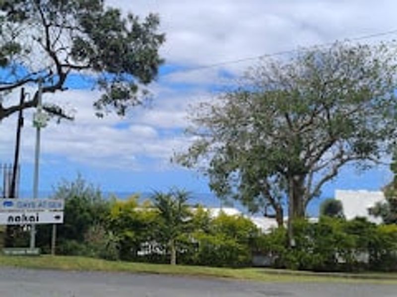 A street-level view of the property frontage featuring mature trees and local signage, with a glimpse of the surrounding landscape.
