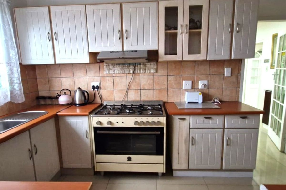 A functional kitchen featuring white cabinetry, laminate countertops, a gas stove with extractor fan, and tiled splashbacks.
