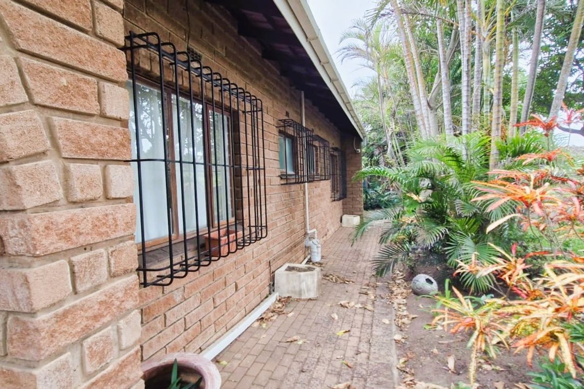 A side view of the property featuring face brick exterior walls, security bars on windows, and a paved walkway leading along the building.