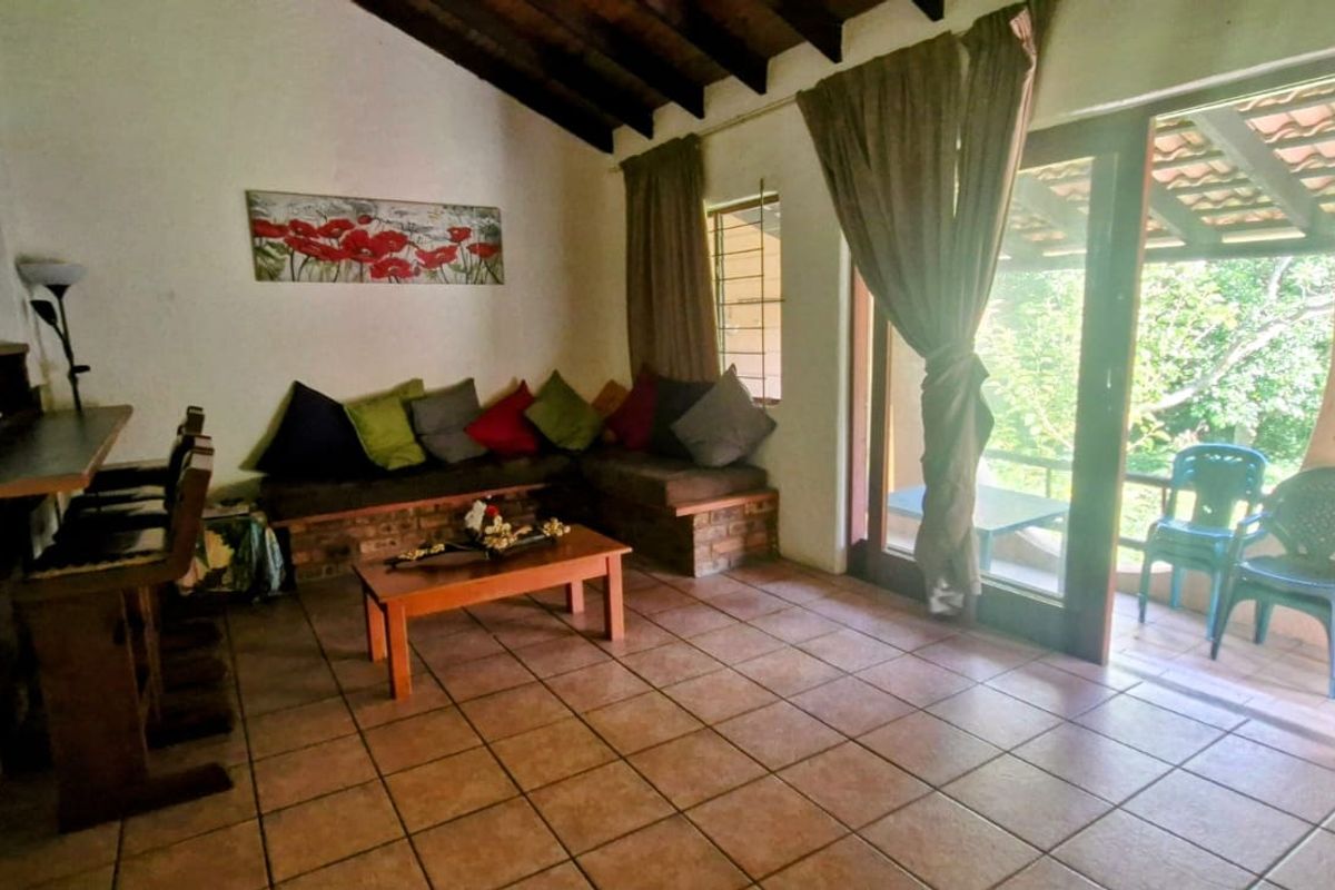 Living room featuring exposed timber ceiling beams, tiled flooring, and a built-in brick seating area with direct access to an outdoor patio.