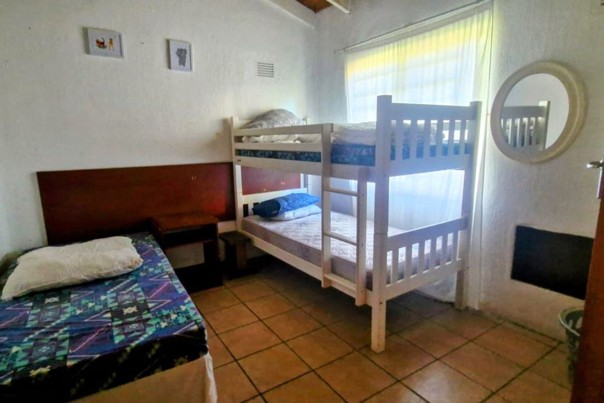 A compact bedroom featuring tiled flooring and exposed beam ceilings, currently configured with multiple sleeping arrangements.