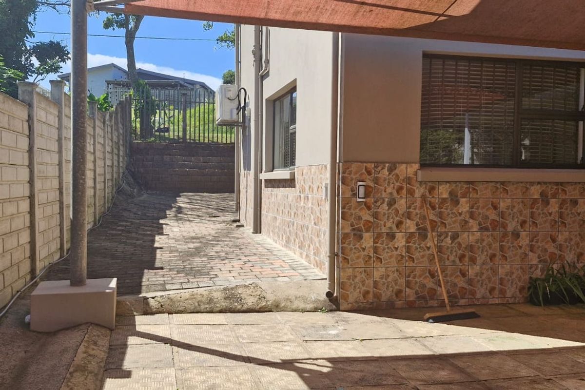 Rear exterior area featuring a paved patio, precast boundary wall, and tiled wall accents, providing a functional outdoor space with a shade sail.