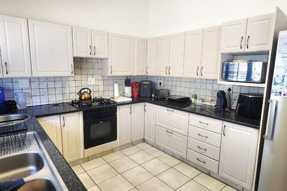 Functional kitchen featuring light-toned cabinetry, granite countertops, a gas hob, built-in oven, and a double stainless steel sink with tiled backsplash.