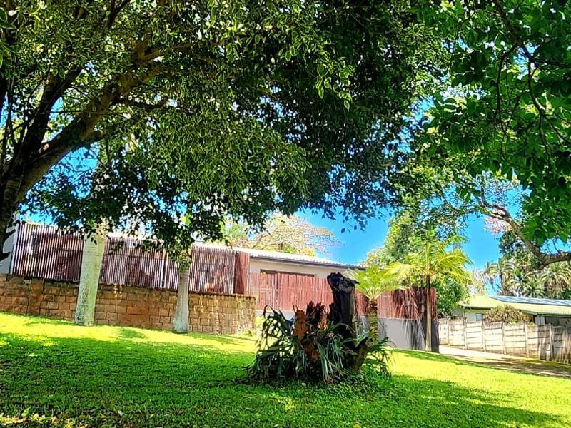 A spacious garden area featuring a stone retaining wall, timber slat fencing, and mature trees providing shade over a well-maintained lawn.