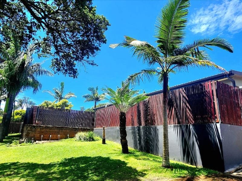 A well-maintained rear garden area featuring timber slat fencing, a retaining wall, and established palm trees under a clear blue sky.