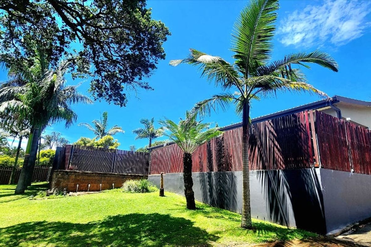 A well-maintained rear garden area featuring timber slat fencing, a retaining wall, and established palm trees under a clear blue sky.