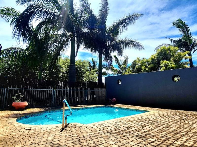 Outdoor pool area featuring a paved deck, boundary wall, and metal fencing, surrounded by mature palm trees.