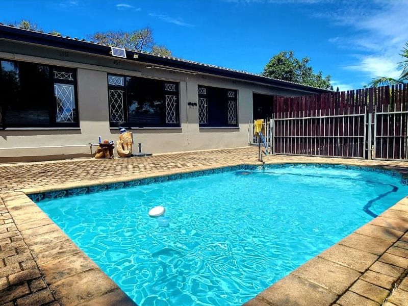 A well-maintained outdoor pool area featuring a paved deck, security fencing, and direct access to the rear elevation of the house.