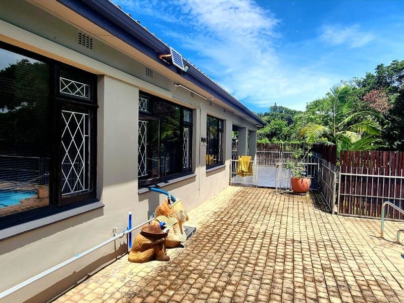 Rear exterior view featuring a paved patio area, swimming pool, and secure perimeter fencing.