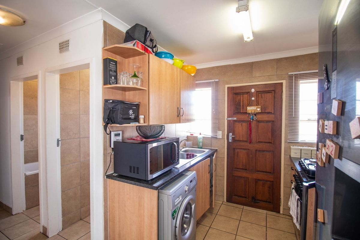 Functional kitchen featuring laminate cabinetry, granite countertops, tiled splashbacks, and integrated cooking appliances, with direct access to the exterior and adjacent bathroom.