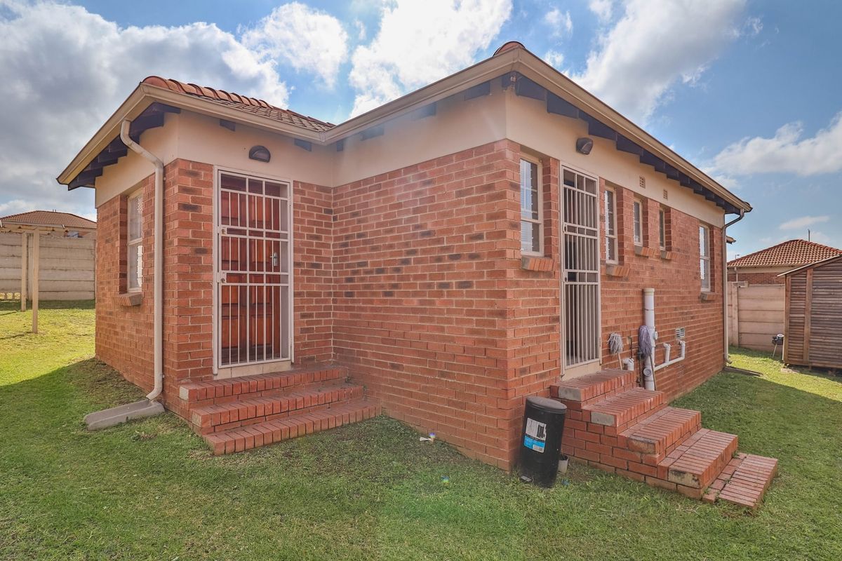 Rear view of a face brick townhouse featuring dual access points with security gates, brick steps, and a surrounding lawn area.