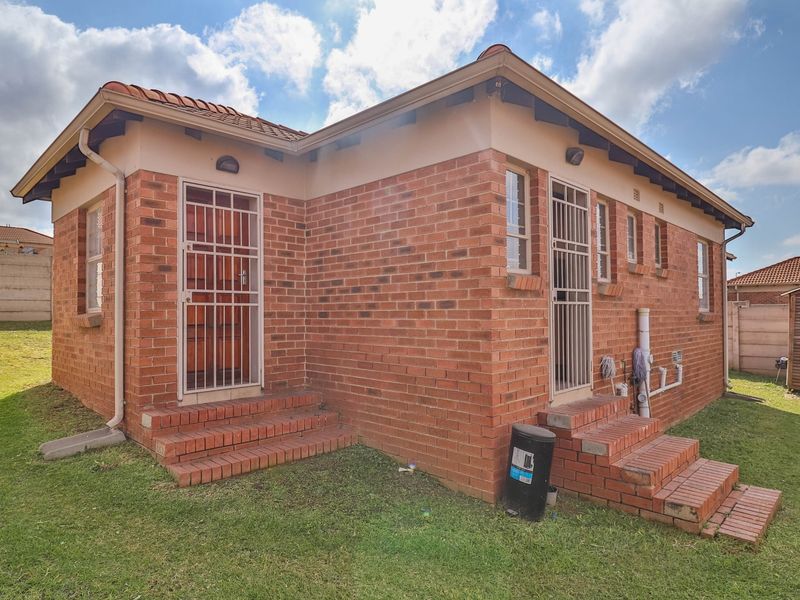 Rear view of a face brick townhouse featuring dual access points with security gates, brick steps, and a surrounding lawn area.