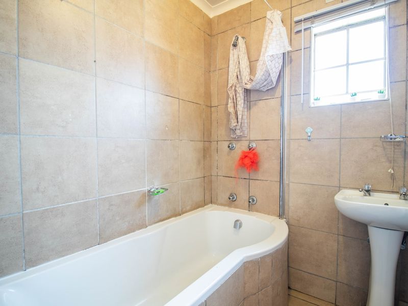 A functional bathroom featuring a bathtub with shower attachment, pedestal basin, and neutral wall tiling, offering a practical layout for renovation.