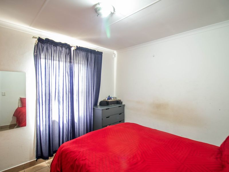 A bedroom featuring tiled flooring, coved ceilings, and a central light fixture, currently showing visible wall staining and surface wear.