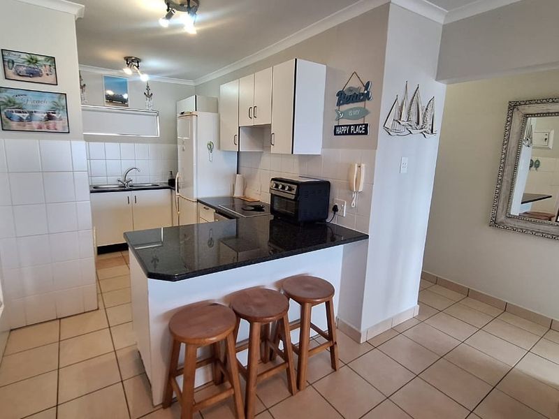 A functional kitchen featuring granite countertops, white cabinetry, a breakfast bar, and tiled flooring, offering a practical layout for daily use.