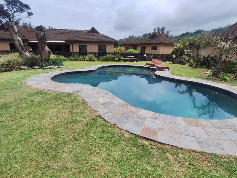 A well-maintained outdoor pool area featuring a kidney-shaped swimming pool with stone coping, surrounded by a landscaped garden and residential buildings.