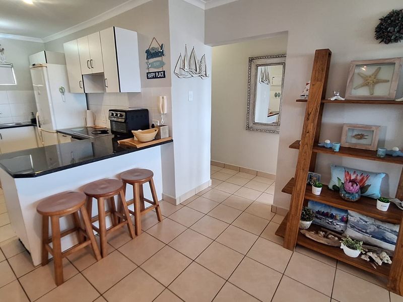 Open-plan kitchen featuring granite countertops, white cabinetry, and ceramic tiled flooring, seamlessly flowing into the adjacent living area.