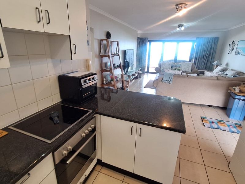 Open-plan living area featuring a functional kitchen with granite countertops, electric hob, and oven, flowing into a spacious lounge with access to a balcony.