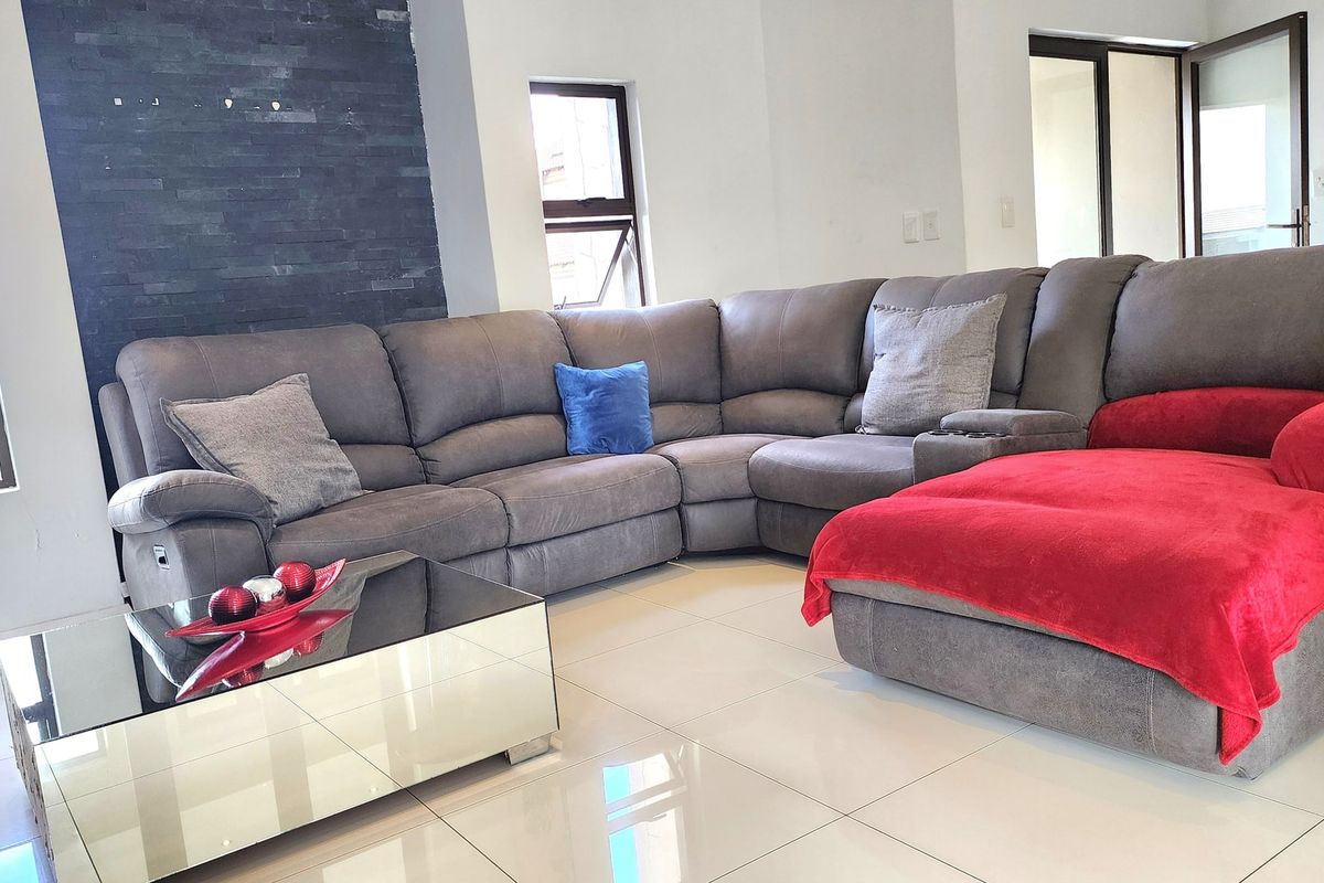 A bright living room featuring large format floor tiles, a dark stone-clad feature wall, and modern aluminium window frames.