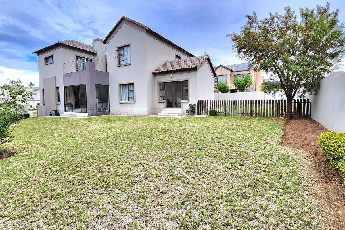 Rear view of a two-story residential house featuring a private garden, balcony, and secure boundary fencing.