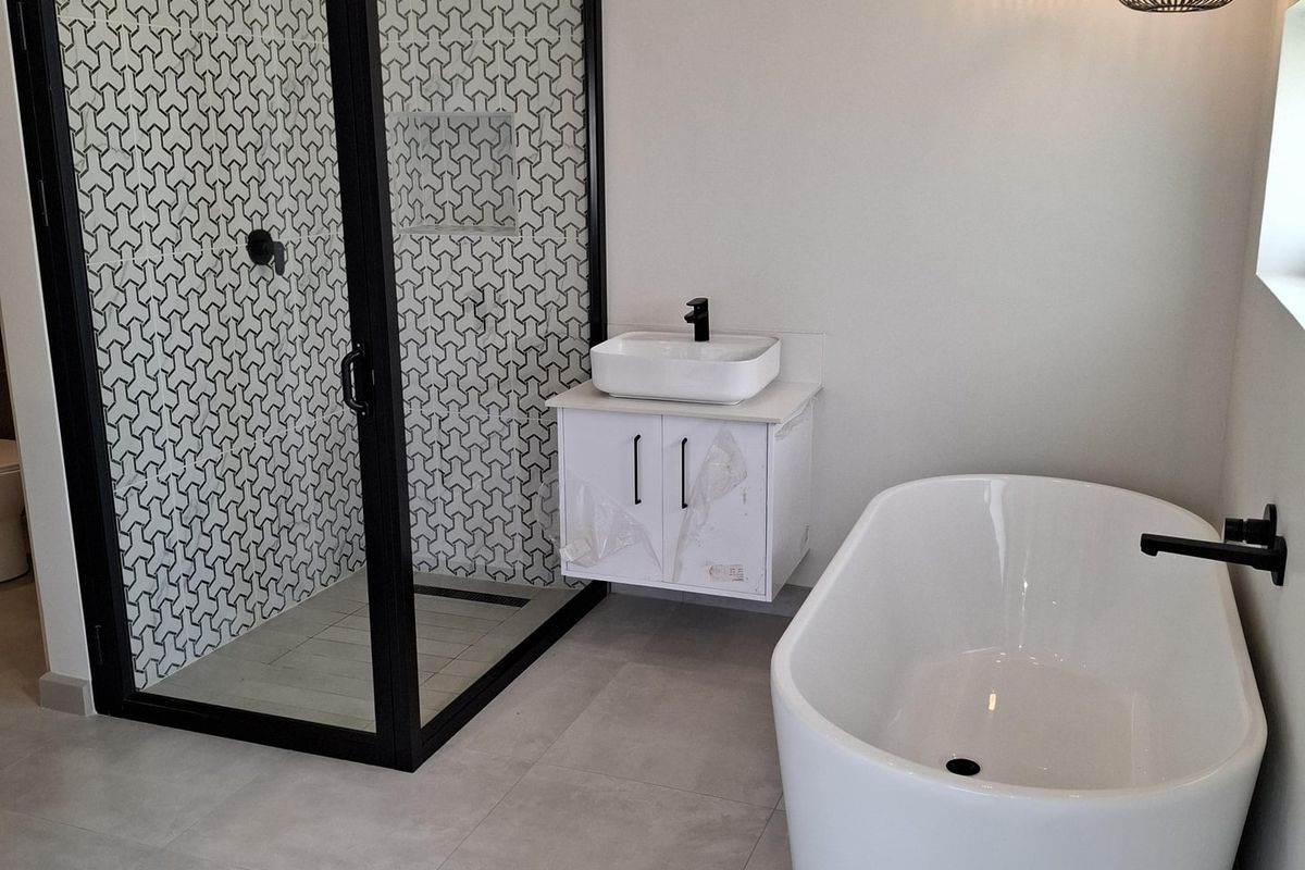Modern bathroom featuring a sleek freestanding bathtub, a walk-in shower with geometric patterned tiles, a wall-mounted vanity, and contemporary black fixtures.