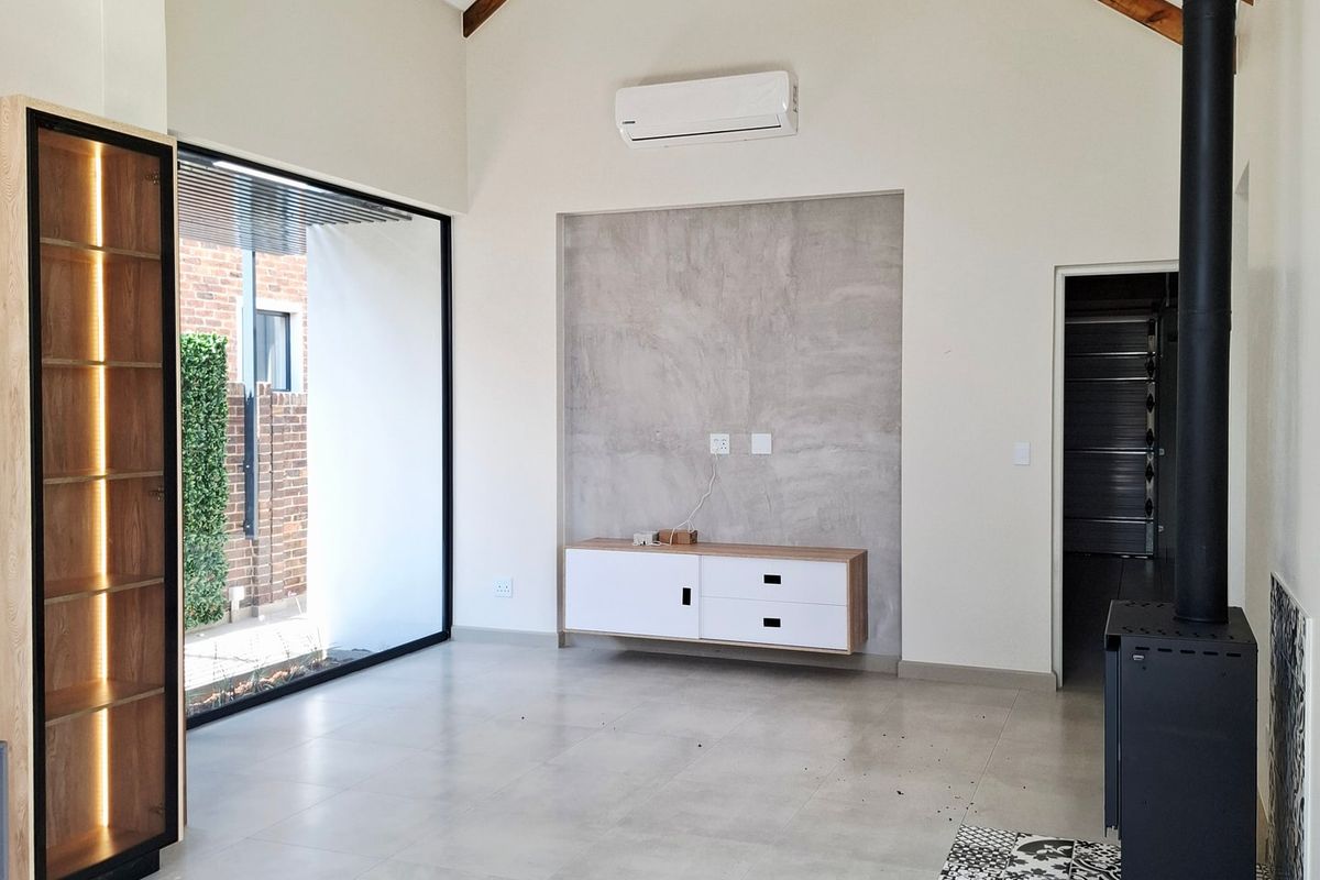 Spacious living room featuring a vaulted ceiling with exposed timber beams, a modern fireplace, tiled flooring, and a large glass door leading outdoors.