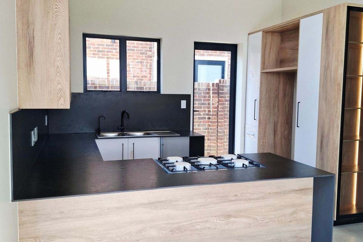 Modern kitchen featuring light wood cabinetry, dark countertops, a gas hob, and high vaulted ceilings with exposed timber beams.