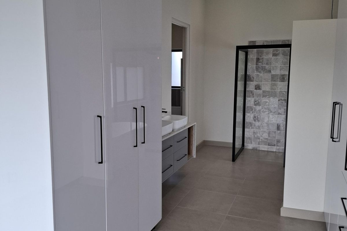 Modern bathroom featuring high-gloss built-in cabinetry, a double vanity, and a walk-in shower with contemporary tiled finishes.