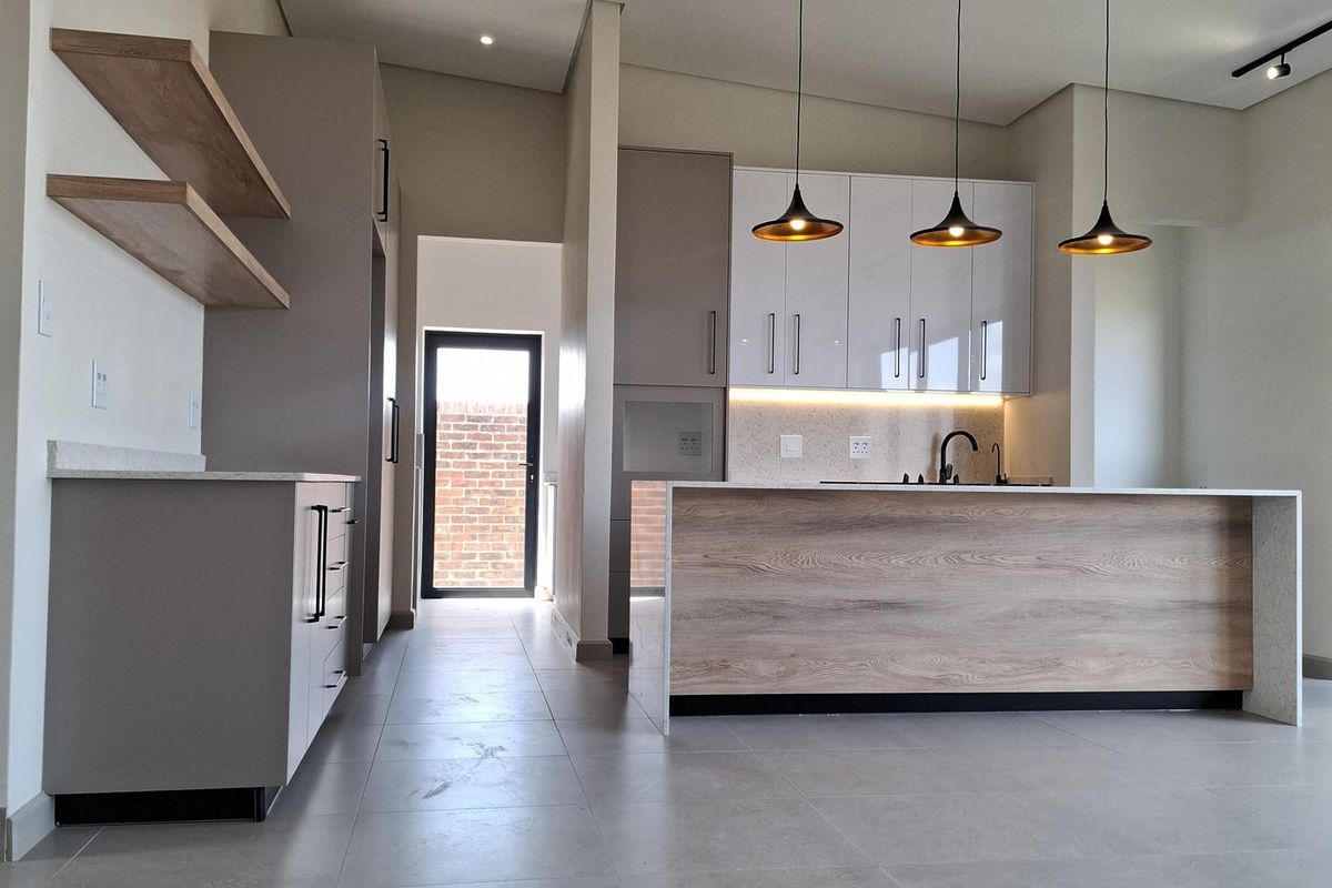 Modern, open-plan kitchen featuring a central island, sleek cabinetry, stone countertops, and contemporary pendant lighting with neutral tiled flooring throughout.