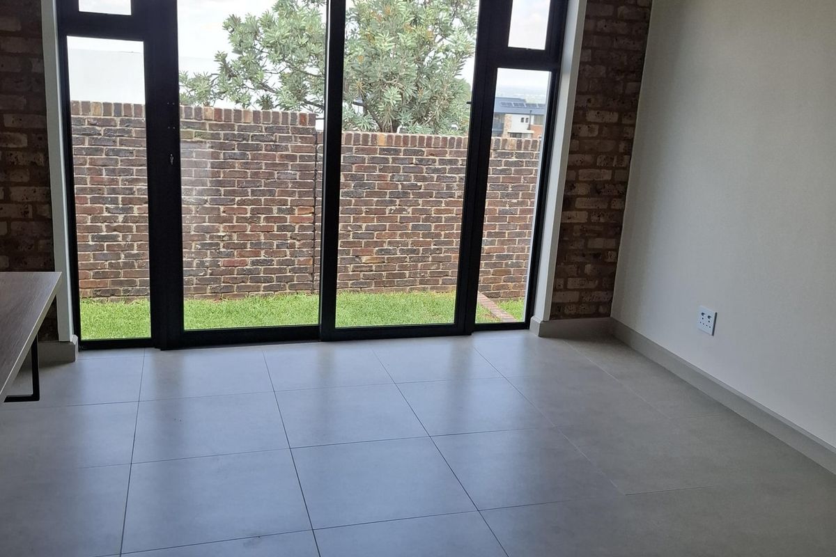 A bright, modern living area featuring large sliding glass doors, exposed brickwork, and neutral floor tiles, offering direct access to the garden.