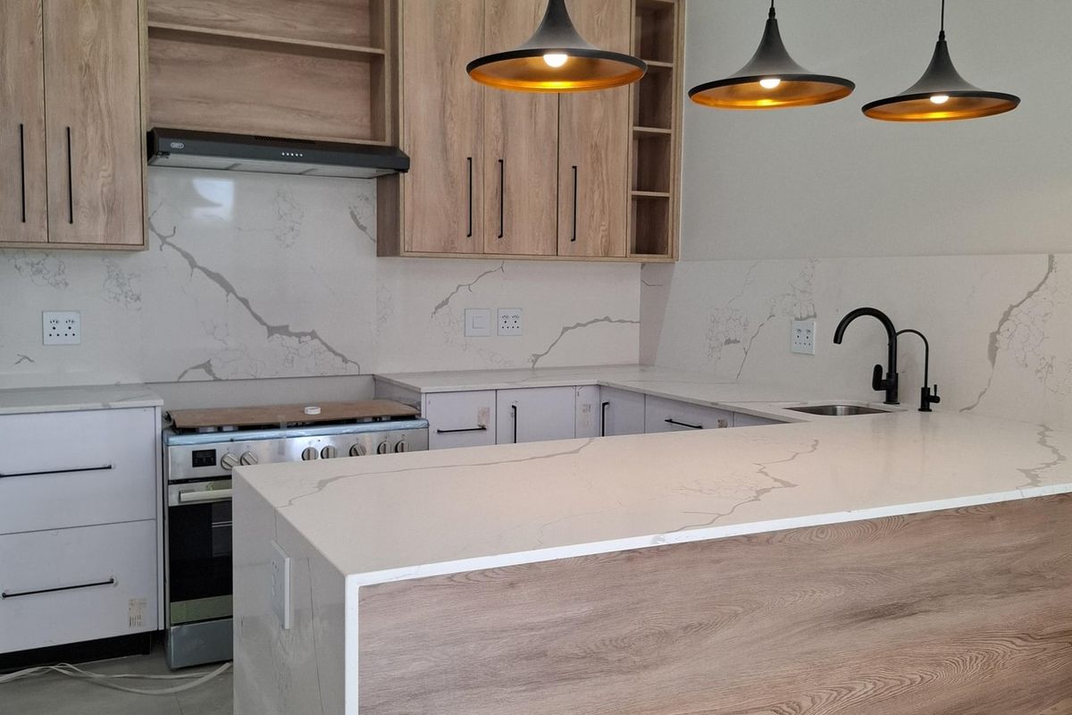 Modern kitchen featuring wood-finish cabinetry, quartz countertops with marble-look backsplash, integrated appliances, and stylish pendant lighting over the central island.