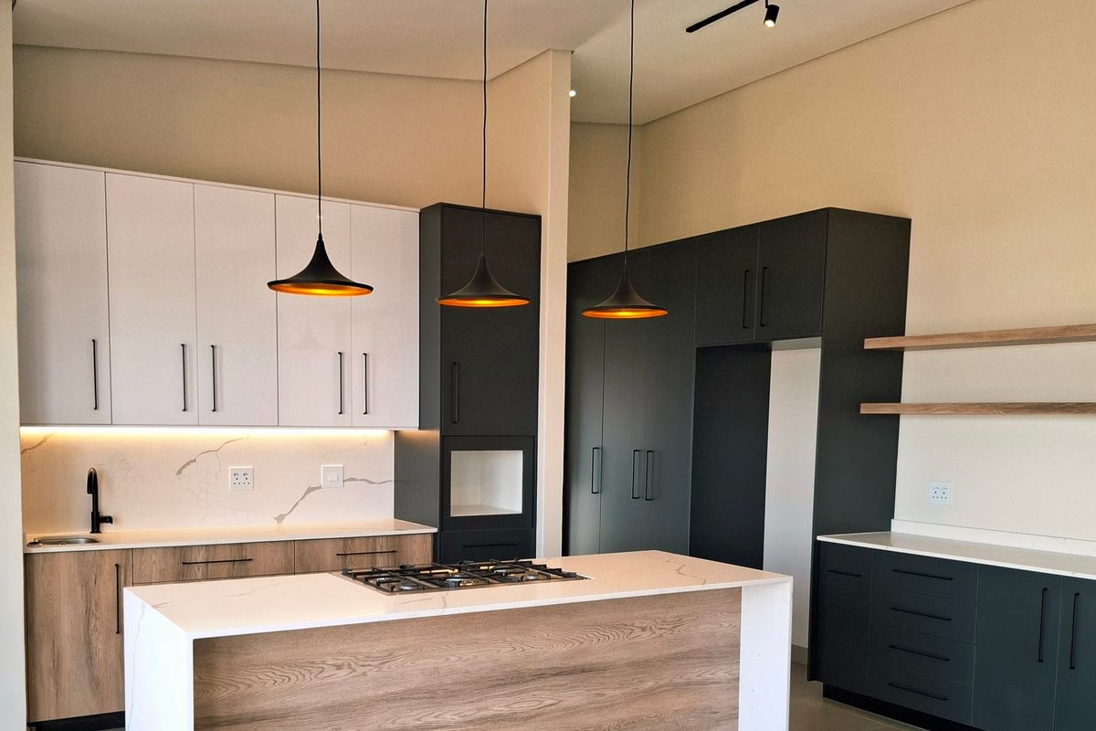 Modern kitchen featuring a large island with a gas cooktop, two-tone cabinetry, stone countertops, and contemporary pendant lighting.
