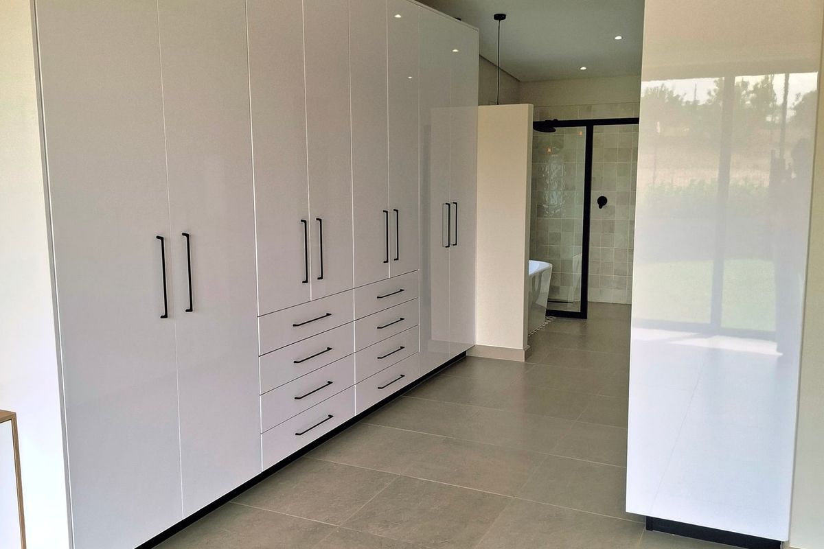 Spacious bedroom featuring extensive modern white built-in cupboards, neutral tiled flooring, recessed lighting, and direct access to an en-suite bathroom.