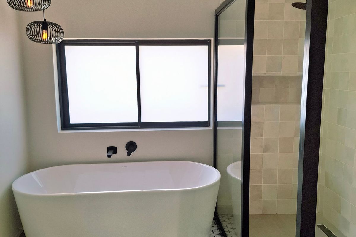 Modern bathroom featuring a sleek freestanding bathtub, a walk-in shower with black metal framing, and contemporary matte black fixtures.